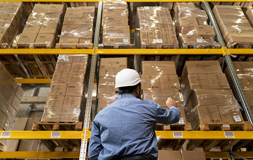 Warehouse worker inspecting inventory on a tall pallet rack